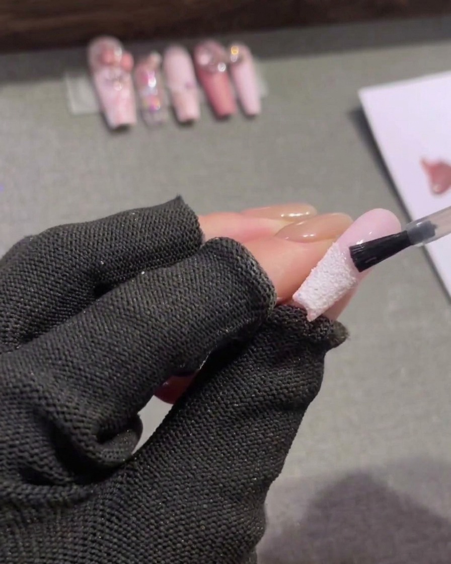 Ein kleiner Pinsel trägt matten Top Coat auf die rosa Fläche oberhalb der weißen French-Spitze auf.