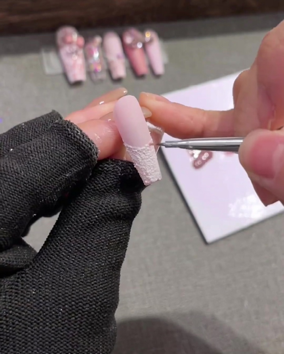 Nahaufnahme eines Liners, der zarte, hellrosa vertikale Streifen über eine strukturierte weiße French-Spitze zieht.