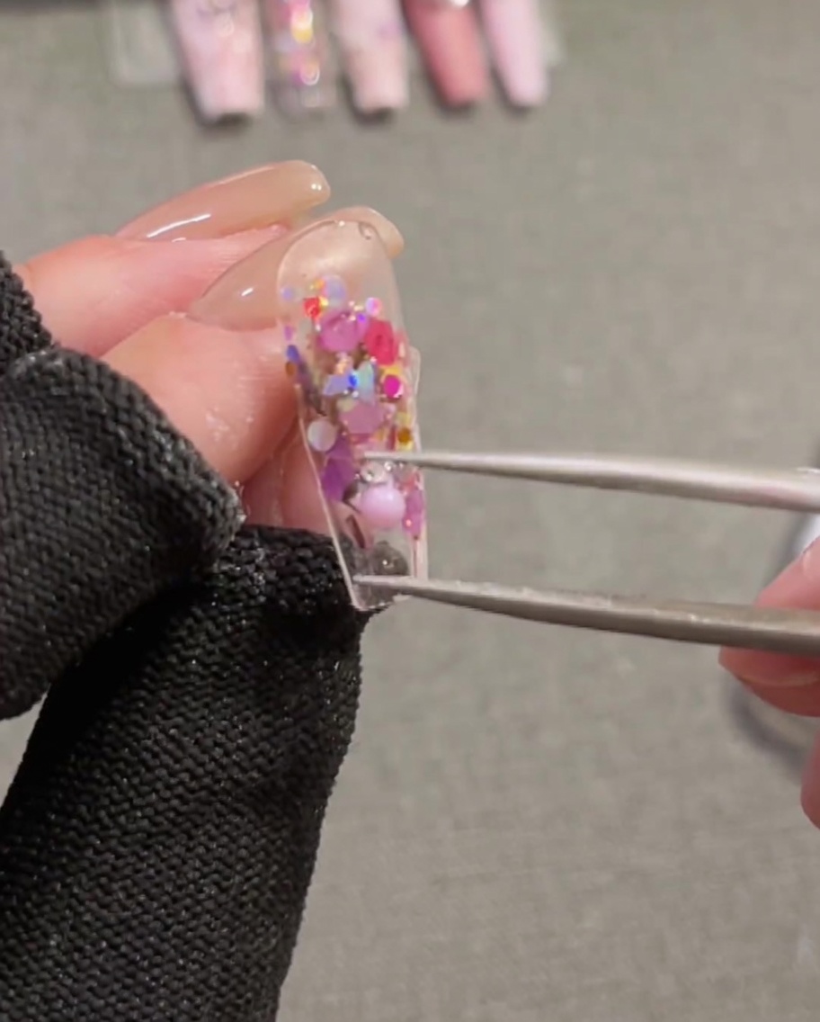 Eine Pinzette positioniert eine pinke 3D-Schleife auf einem Nagel mit feuchtem Aufbaugel.