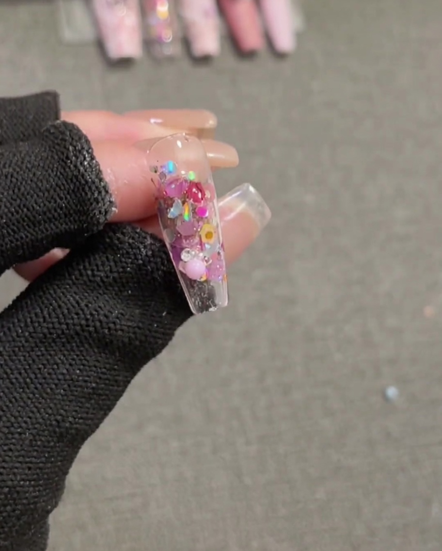 Ein Pinsel trägt Top Coat auf einen Nagel mit eingebetteten Pailletten und einer 3D-Schleife auf.