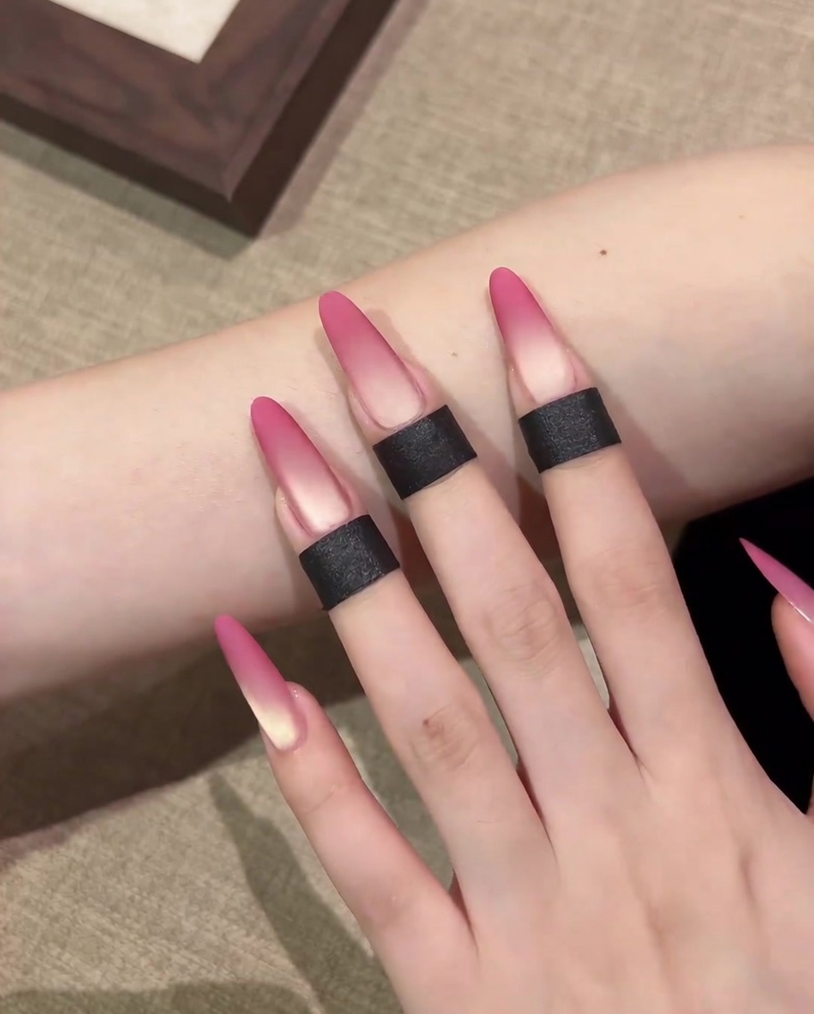 Nahaufnahme eines Make-up-Schwämmchens, das pinkes Cat-Eye-Gel auf die Nagelspitze aufträgt.