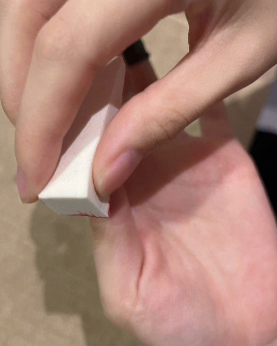 Eine Hand, die mit einem Schwämmchen Gel auf den Nagel tupft, bevor es unter der UV-Lampe härtet.