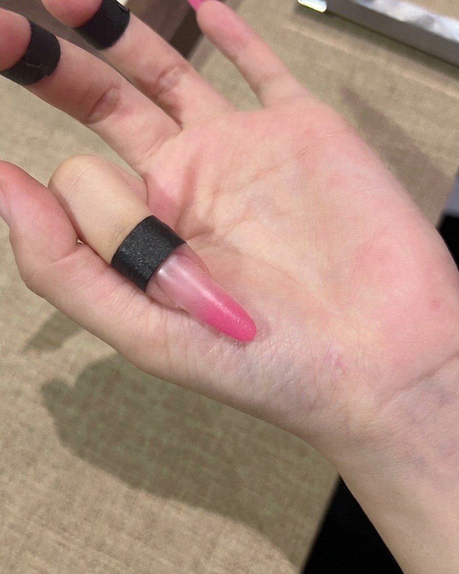 Ein Pinsel trägt eine Schicht pinkes Cat-Eye-Gel auf die gesamte Oberfläche eines Nagels auf.