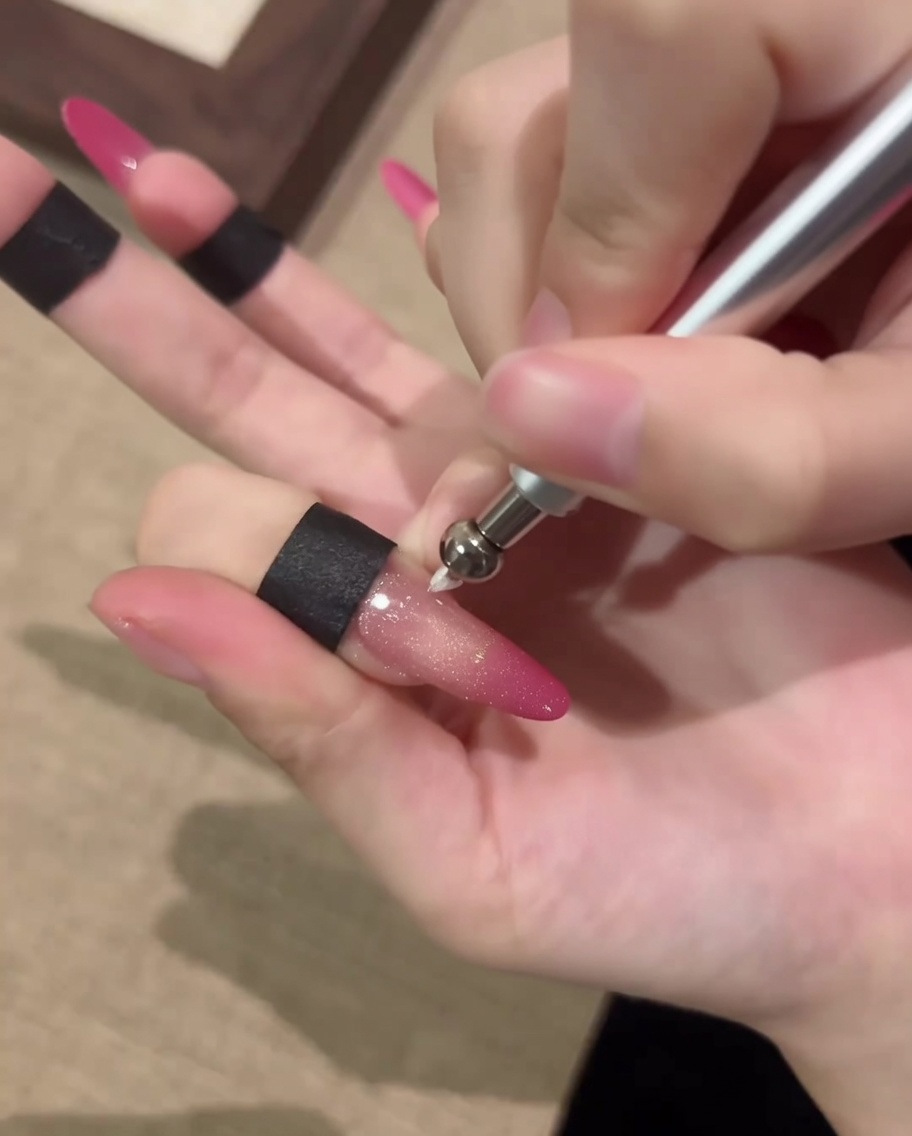 Nahaufnahme eines Nagels, der mit einem magnetischen Stiftwerkzeug bearbeitet wird, um einen kreisförmigen Cat-Eye-Orbeffekt zu erzeugen.