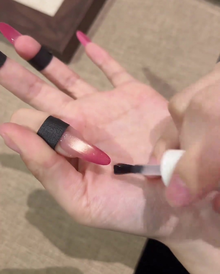 Ein Pinsel trägt einen klaren matten Überlack auf ein fertiges Cat-Eye-Nageldesign auf.