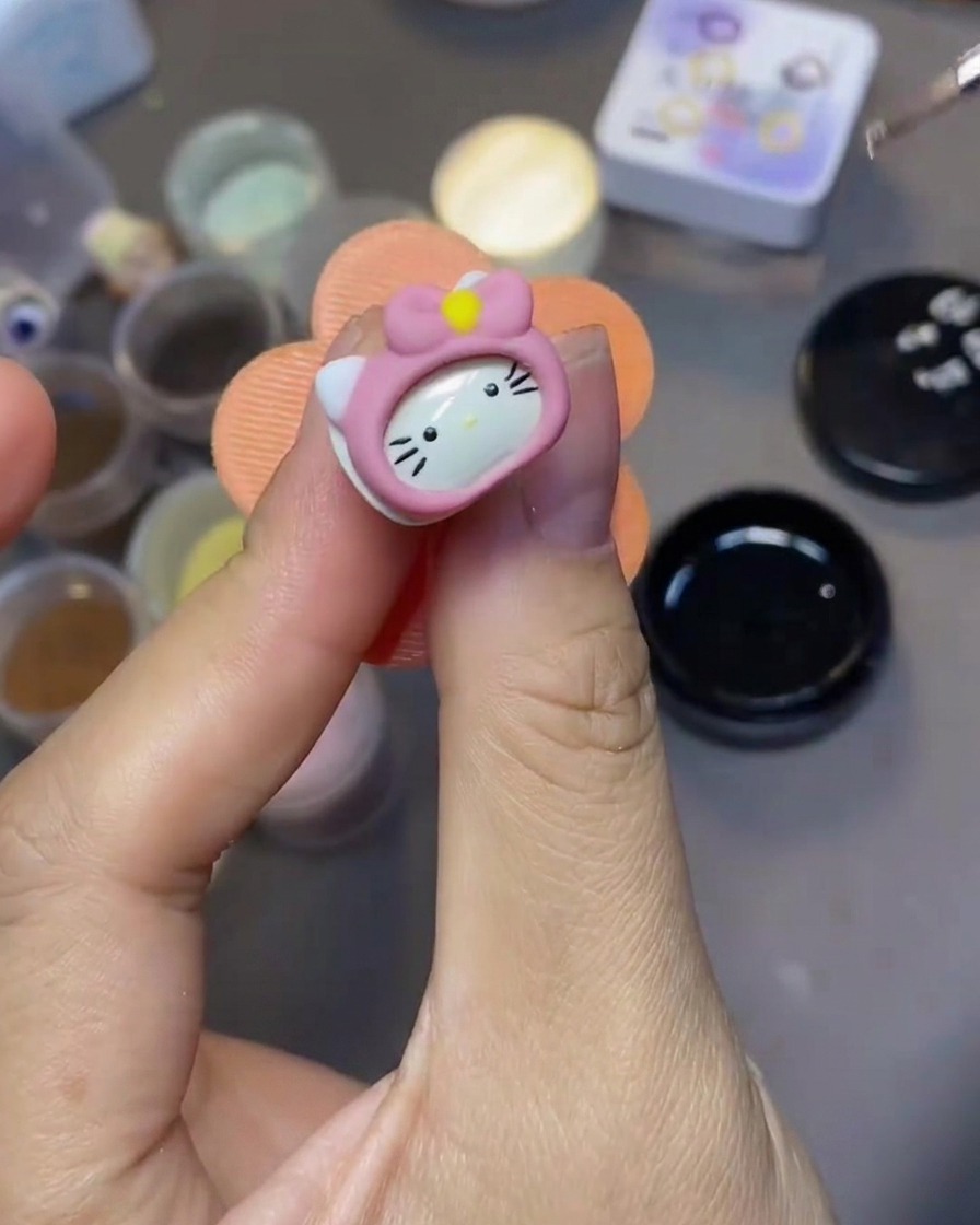 Ein feiner Nail-Art-Pinsel trägt klaren Top Coat über einen 3D Hello Kitty Nagelanhänger auf.