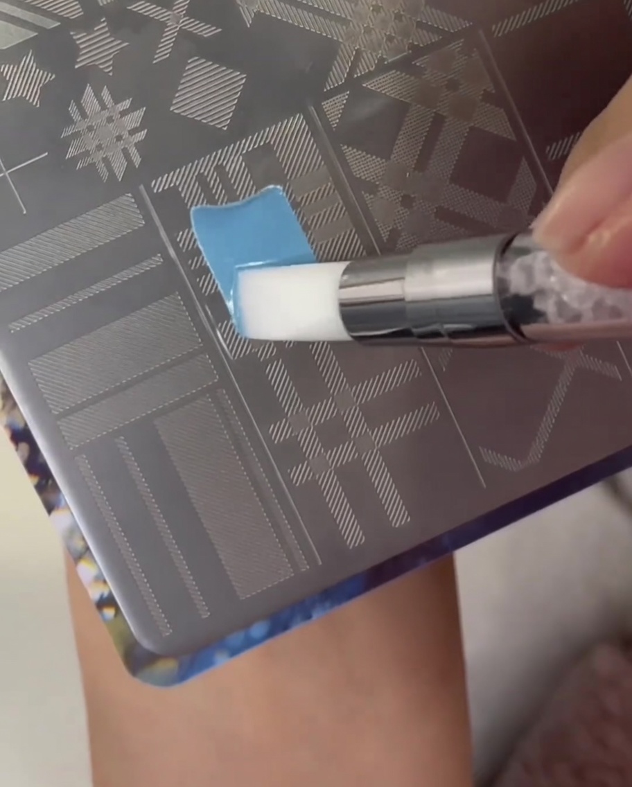 Ein Pinsel trägt hellblauen Lack über einen Plaid-Musterabschnitt auf einer Metall-Stamping-Platte auf.