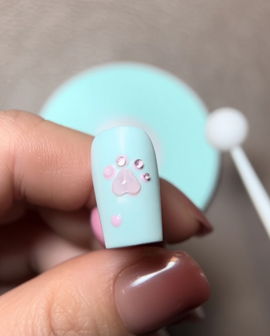 Nahaufnahme eines Pinsels, der ein Tröpfchen Modelliergel auf das 3D-Pfotendesign auf dem Nagel gibt.