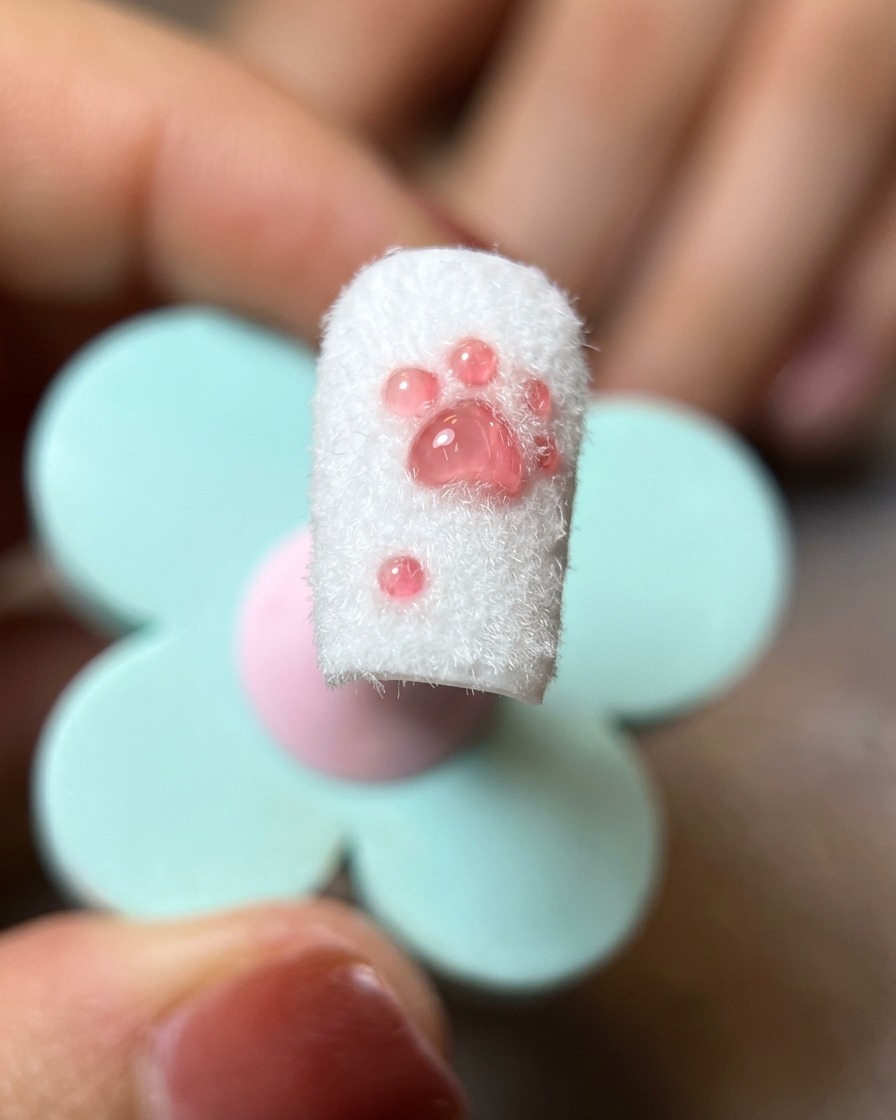Nahaufnahme eines fertigen Katzenpfoten-Nageldesigns, bei dem überschüssiges Flocking-Puder mit einem weichen Pinsel entfernt wird.