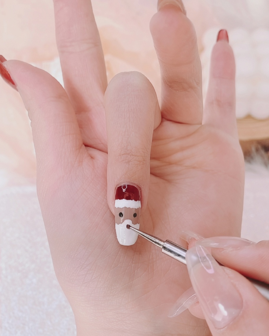 Ein feiner Liner-Pinsel setzt zwei winzige schwarze Punkte als Augen auf den Nagel.