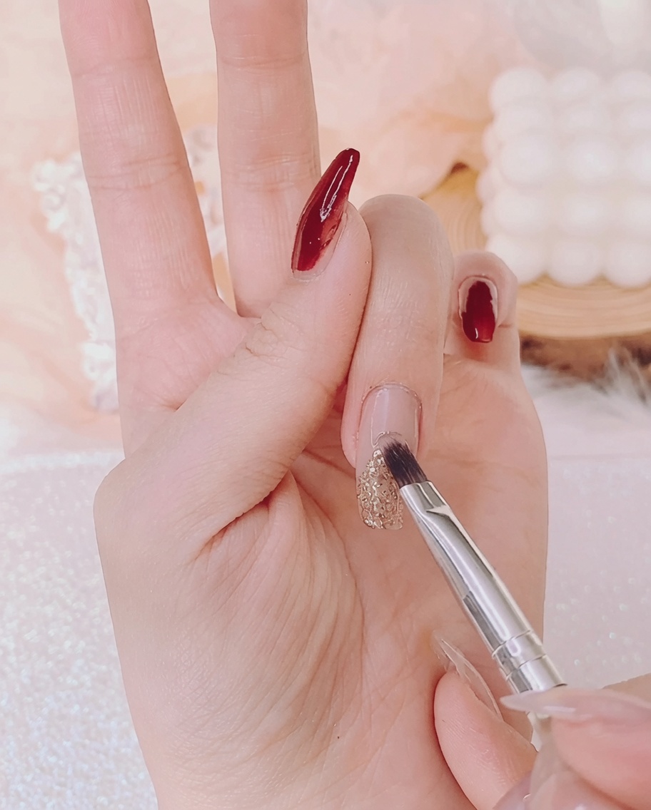 Ein Nagelpinsel verteilt dicken, transparenten Strass-Kleber über dem goldenen Weihnachtsbaum-Design.
