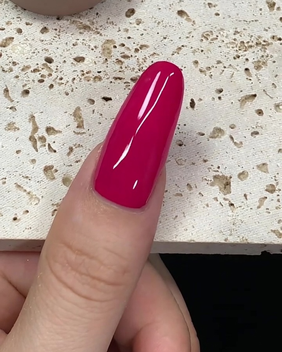 Ein mit tiefrotem Gellack beladener Pinsel schwebt nahe der Nagelhaut.