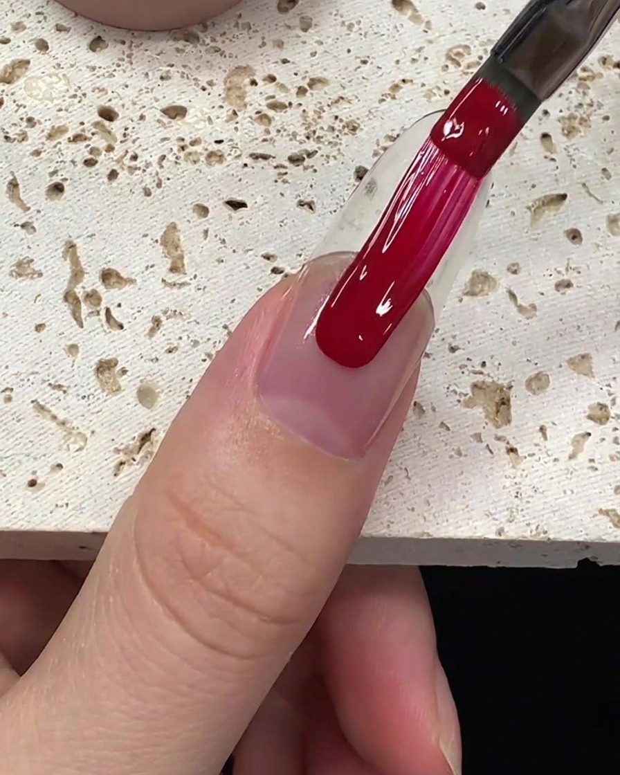 Ein gleichmäßiger Auftrag von tiefrotem Gellack wird über die Nagelplatte nach unten gezogen.
