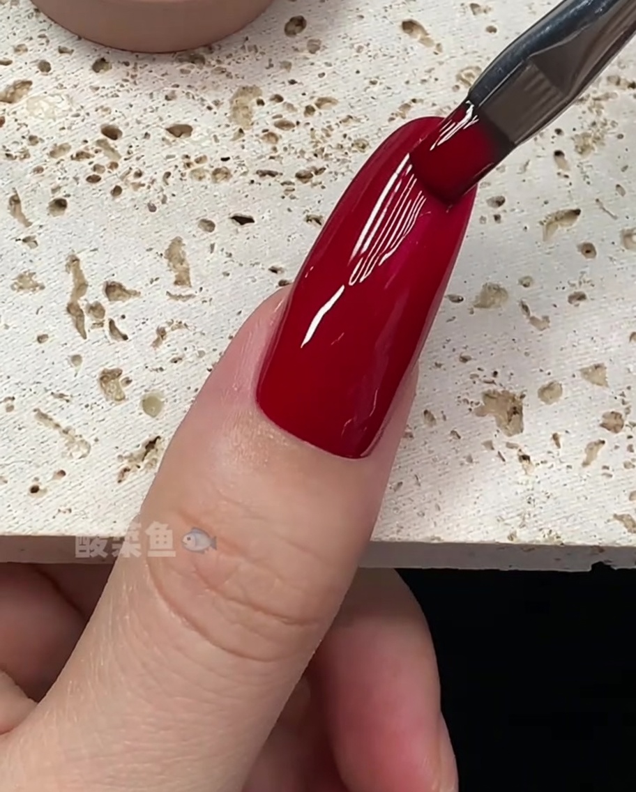 Nahaufnahme eines Pinsels, der die Ränder eines mit tiefrotem Gellack überzogenen Nagels perfektioniert.