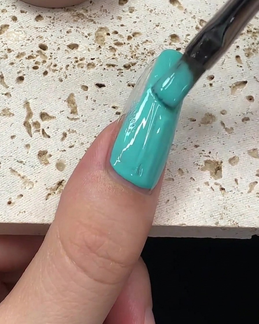 Ein Pinselstrich mit mintgrünem Gellack wird in der Mitte des Nagels nach unten gezogen.