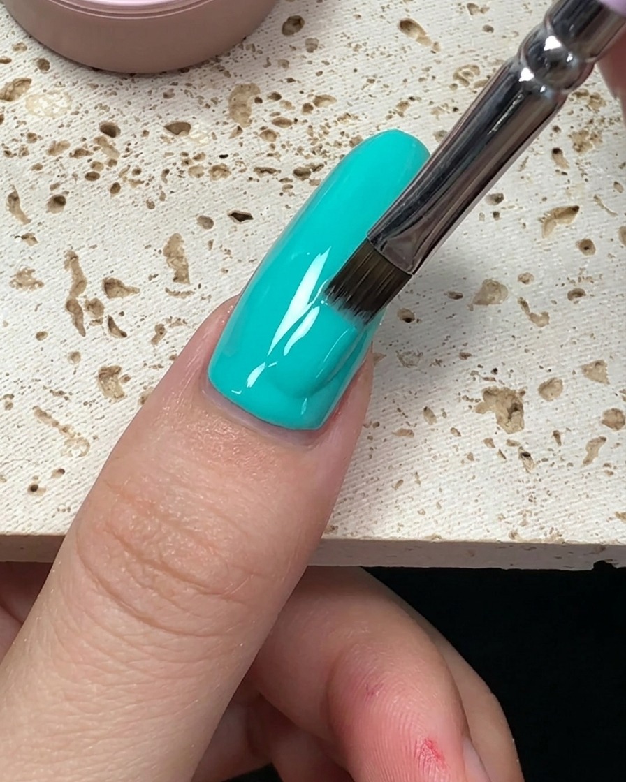Nahaufnahme der letzten Pinselstriche, die den mintgrünen Gellack bis zum Ende des Nagels glätten.