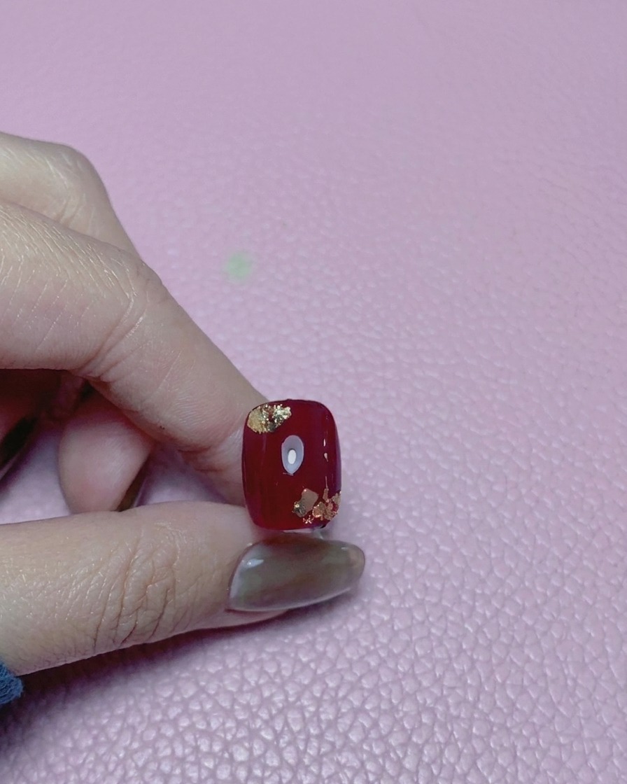 Nahaufnahme eines roten Nagels mit Goldakzenten, überzogen mit einem hochglänzenden Top Coat.