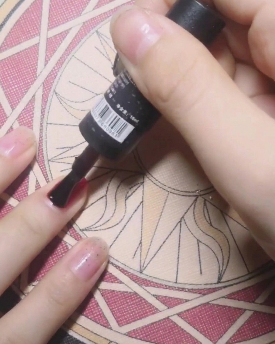 Ein Flaschenpinsel trägt klaren Base Coat auf einen Nagel als Vorbereitung für soliden roten Gellack auf.