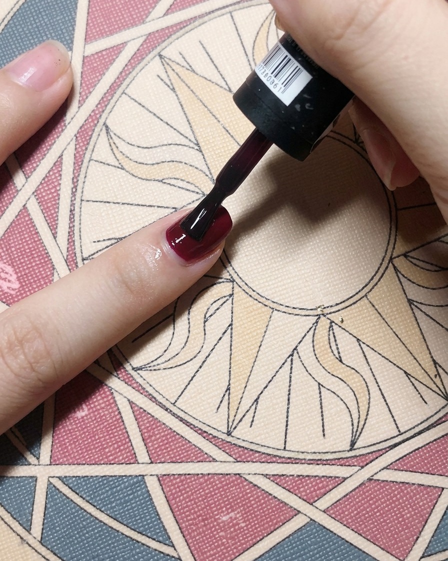 Ein Pinsel trägt einen satten, dunkelroten Gellack über einem Nagel-Base Coat auf und erzeugt eine solide, opake Farbe.