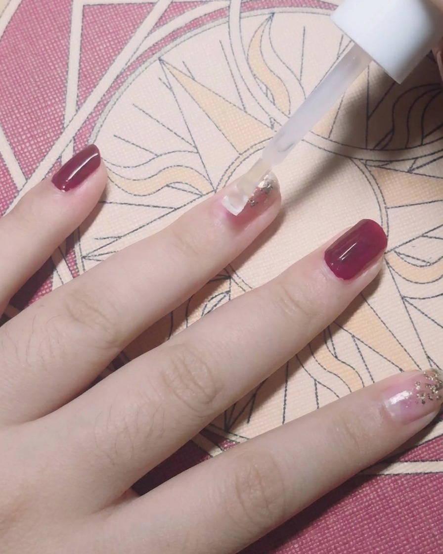 Ein Pinsel trägt einen klaren Top Coat über einen mit Goldfolienflocken verzierten Nagel auf.
