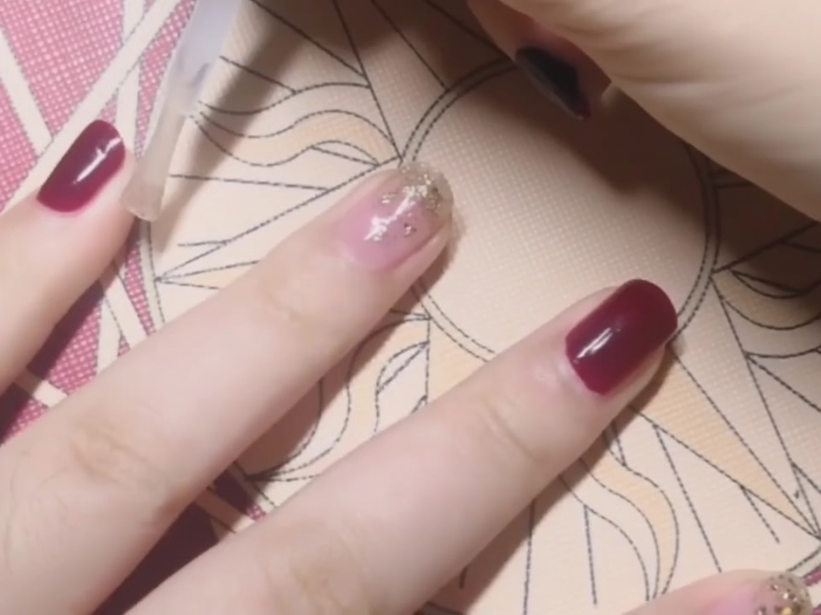 Ein klarer Top Coat wird über einem soliden roten Nagel aufgetragen.