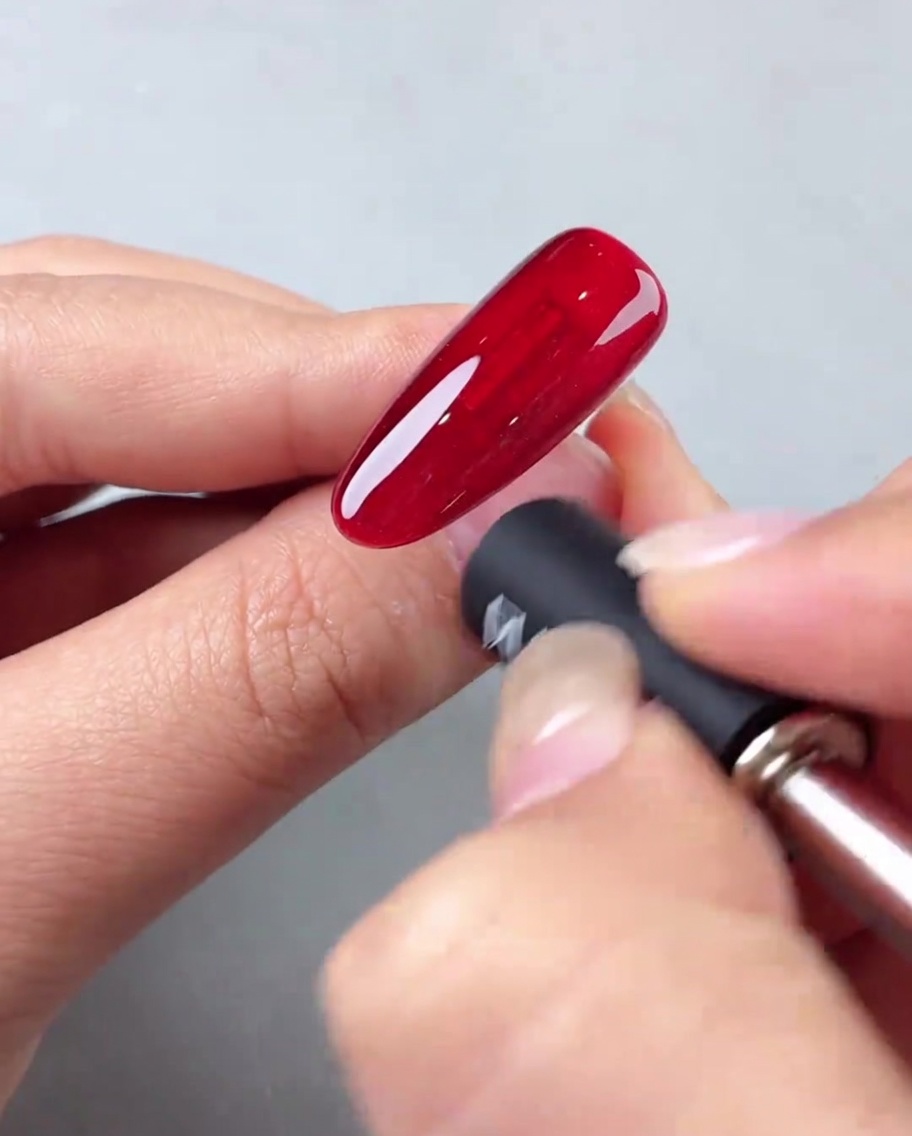 Ein Nagelmagnet wird in einem Winkel an einen roten Cat-Eye-Nagel gehalten, um einen diagonalen Lichteffekt zu erzeugen.
