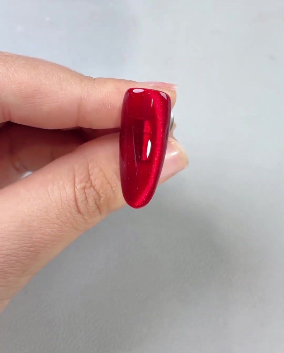Ein glänzender Top Coat wird auf einen fertigen roten Magnetnagel aufgetragen und sorgt für hohen Glanz.