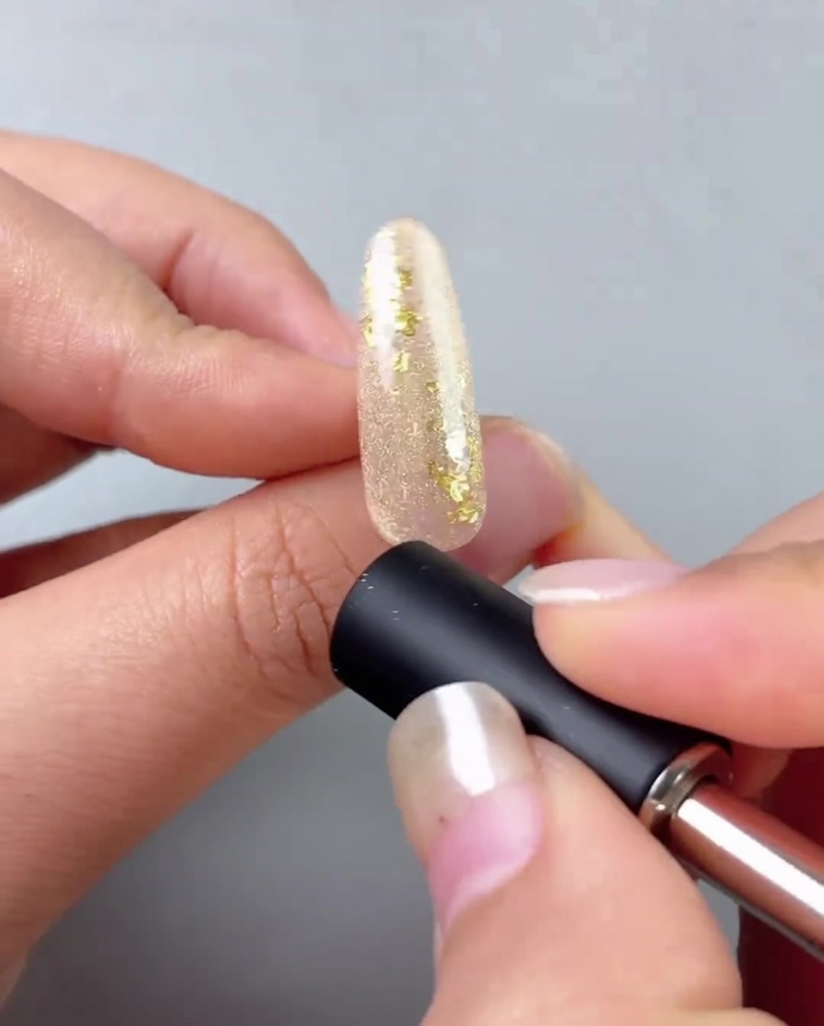Ein Nagelmagnet wird nahe an einen mit Goldgel bemalten Nagel gehalten, um eine reflektierende Cat-Eye-Linie zu erzeugen.