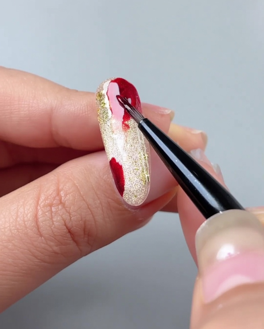 Ein Nagelpinsel verblendet rote Gelflecken mithilfe von Aquarell-Gel zu einem Verlauf.