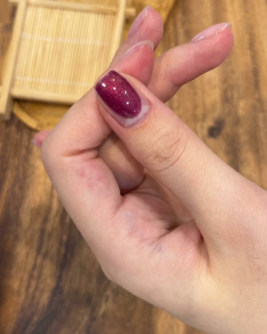 Ein professioneller Nagelpinsel trägt rose-roten magnetischen Gellack gleichmäßig auf.