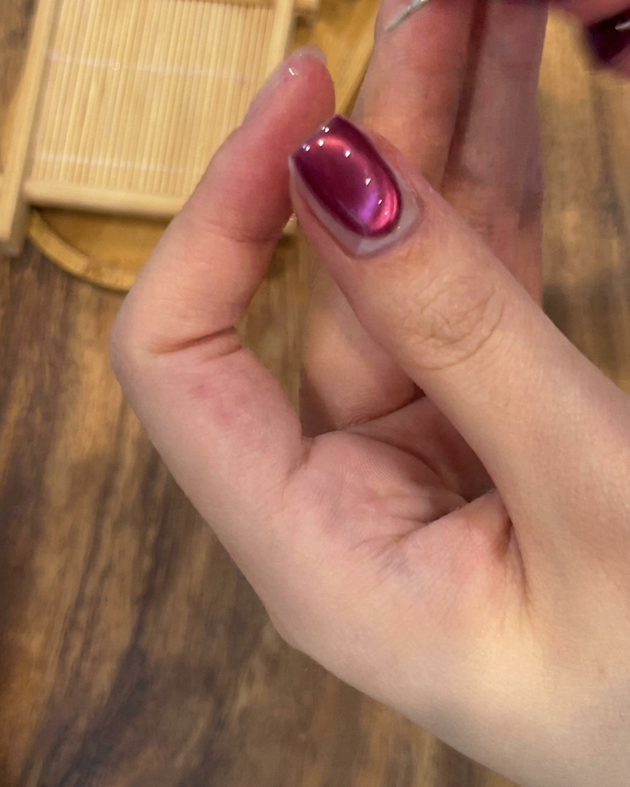 Ein feiner Detailpinsel zeichnet eine zarte Linie mit Silberglitter an die Basis des Nagels.
