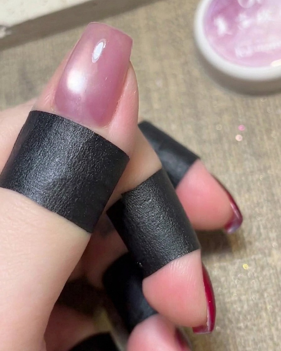 Ein zylindrischer Magnet wird über den noch feuchten, rosa Cat-Eye-Nagellack gehalten.