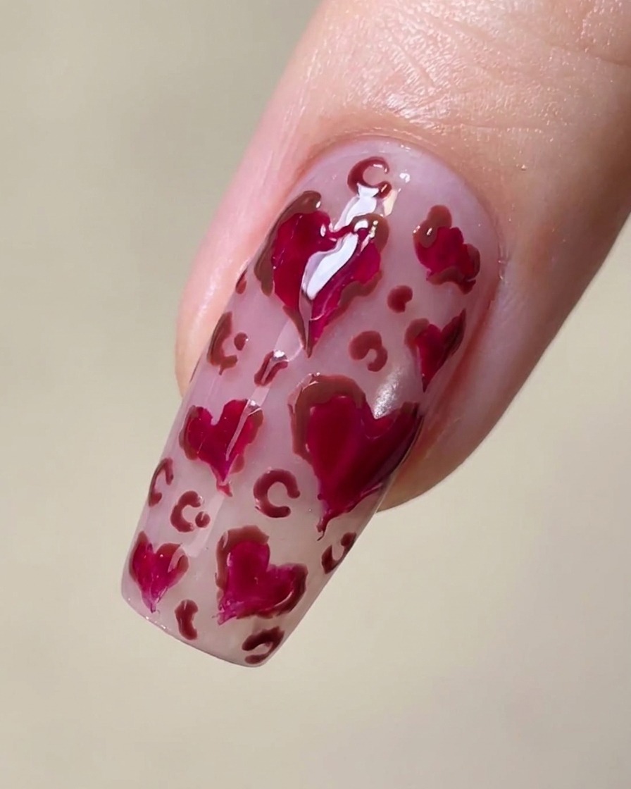 Nahaufnahme eines Nagels mit Magenta-Herzen und feinen braunen Leopardenflecken dazwischen.