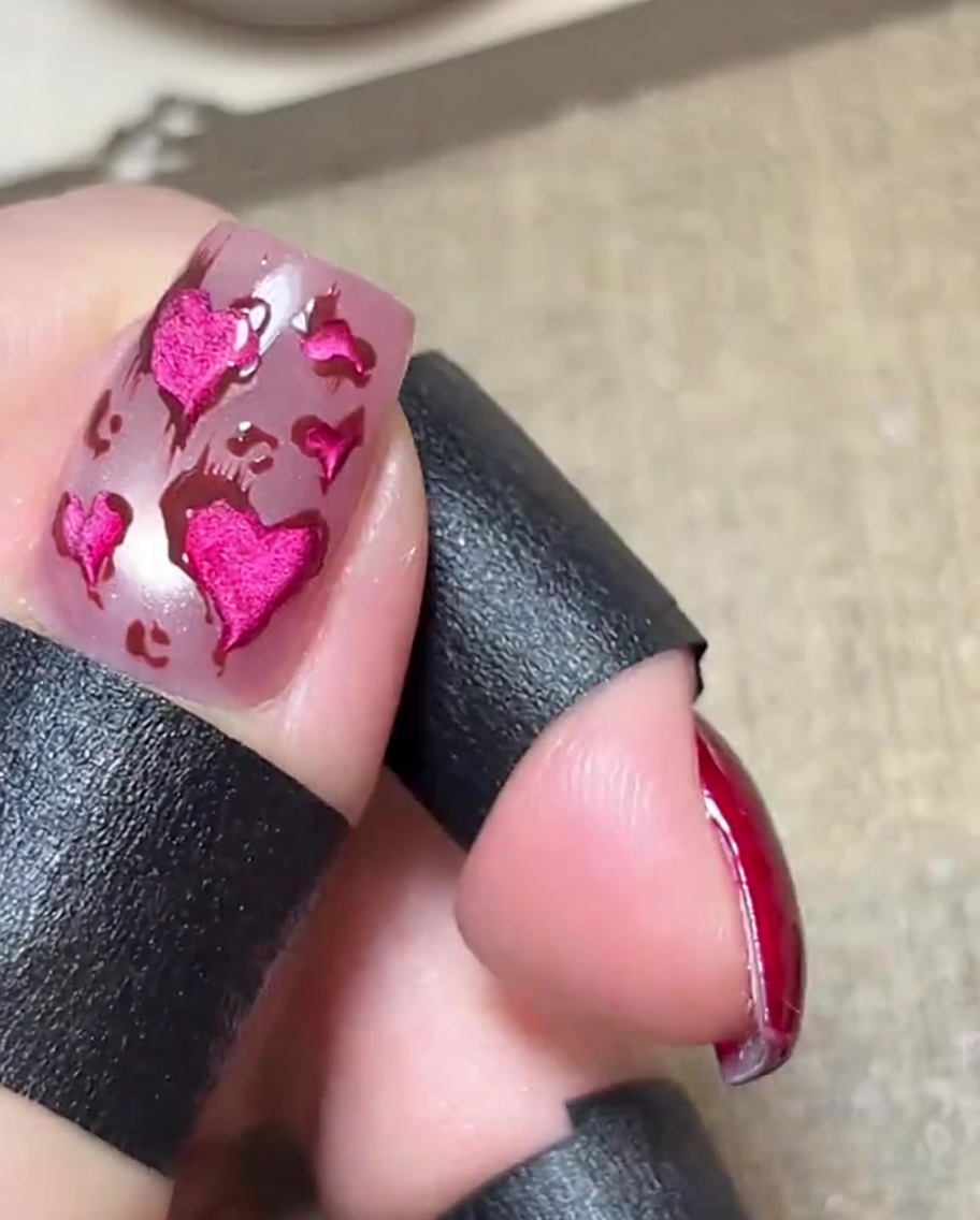 Nahaufnahme eines glänzenden rosa Nagels mit metallisch-pinken Herzen, braunen Konturen und zarten, auslaufenden Linien.