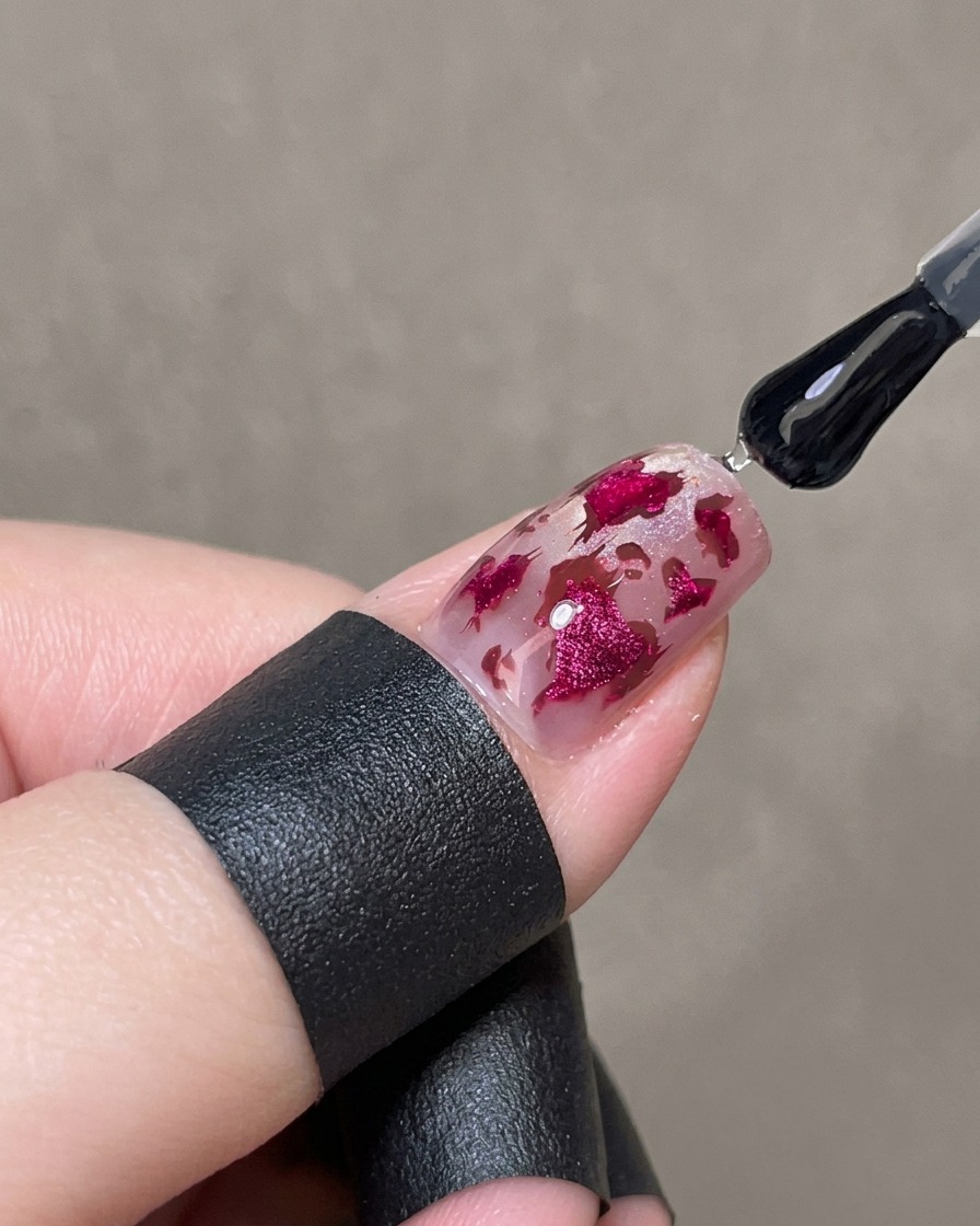 Ein Pinsel trägt eine dicke Schicht klaren Glanzgels über das verzierte Nageldesign auf.