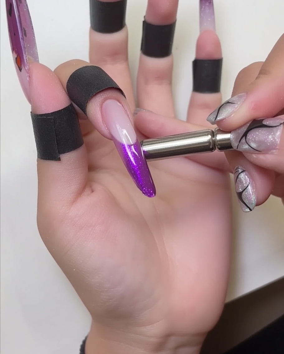 Ein magnetischer Stab wird nahe an die Nagelspitze gehalten, wodurch der schimmernde Effekt im roten Gel sichtbar wird.