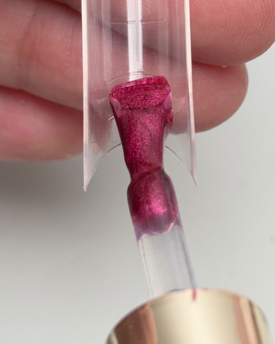 Ein Pinsel trägt magentafarbenes Gel auf eine transparente Nagel-Schablone auf.