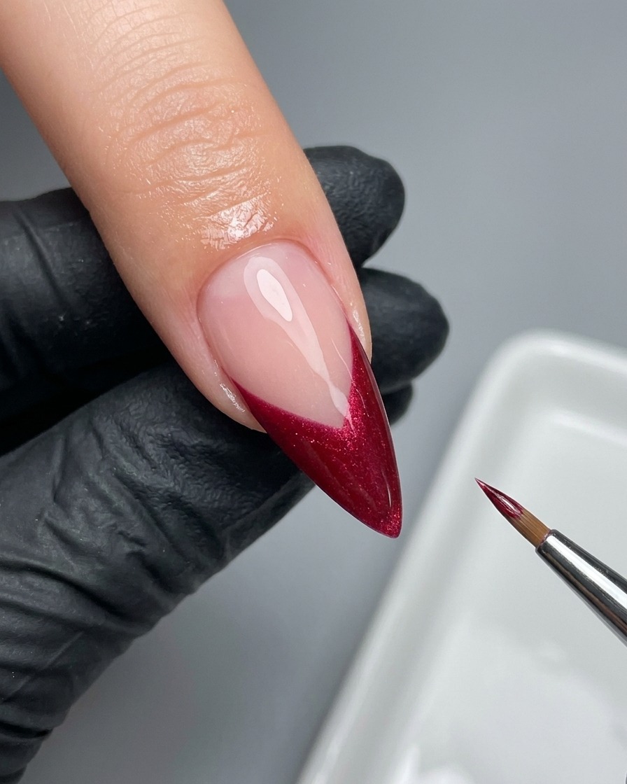 Ein feiner Liner-Pinsel perfektioniert sorgfältig den Rand einer magentafarbenen French Tip.