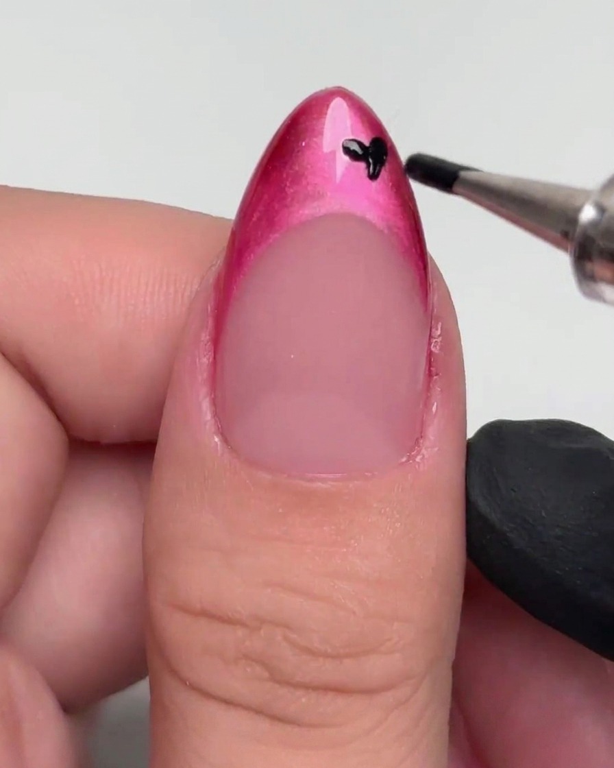 Ein Dotting-Tool setzt kleine schwarze Punkte auf eine magentafarbene French Tip.