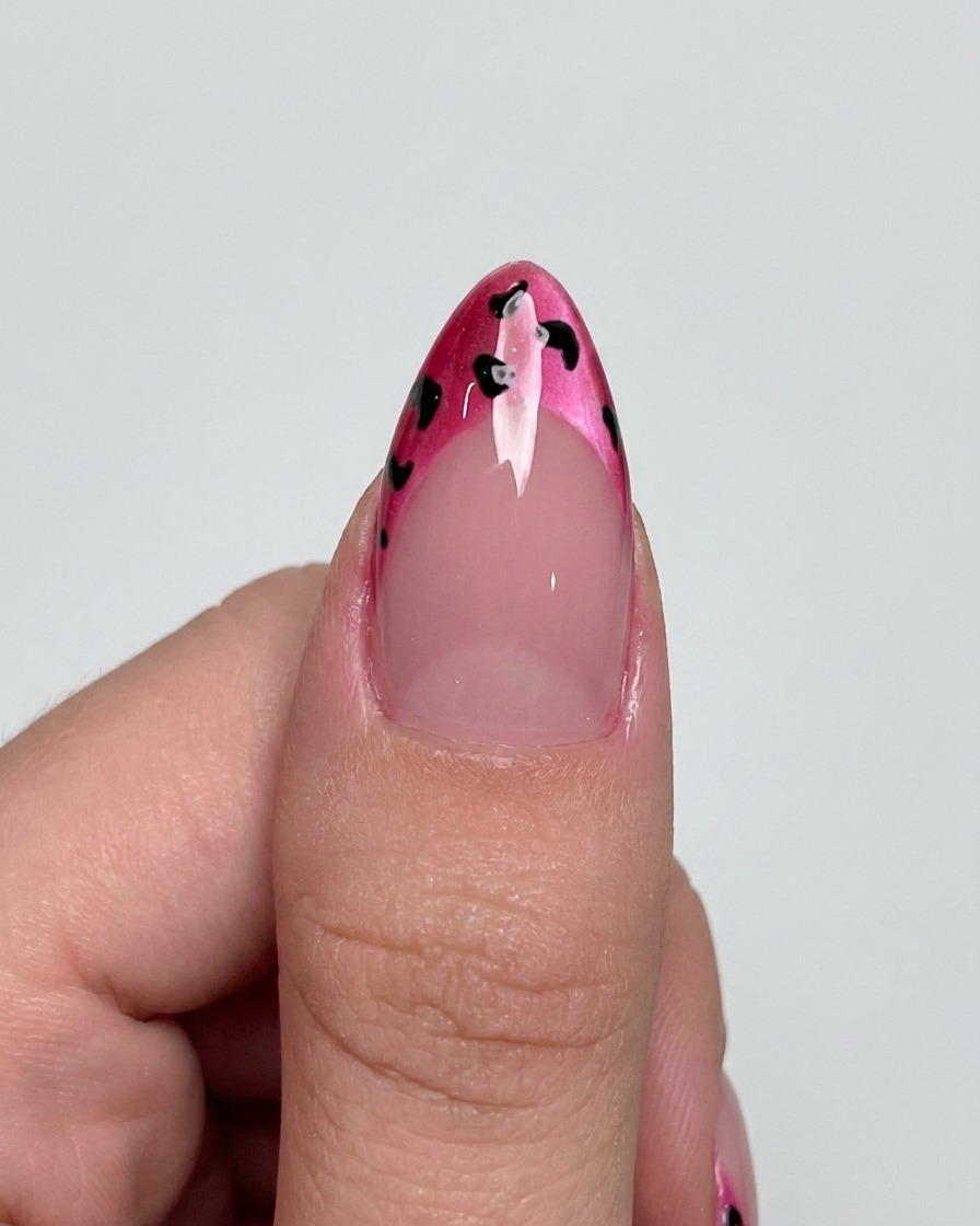 Ein Liner-Pinsel fügt feine schwarze Umrandungen um die Punkte auf einer magentafarbenen French Tip hinzu.