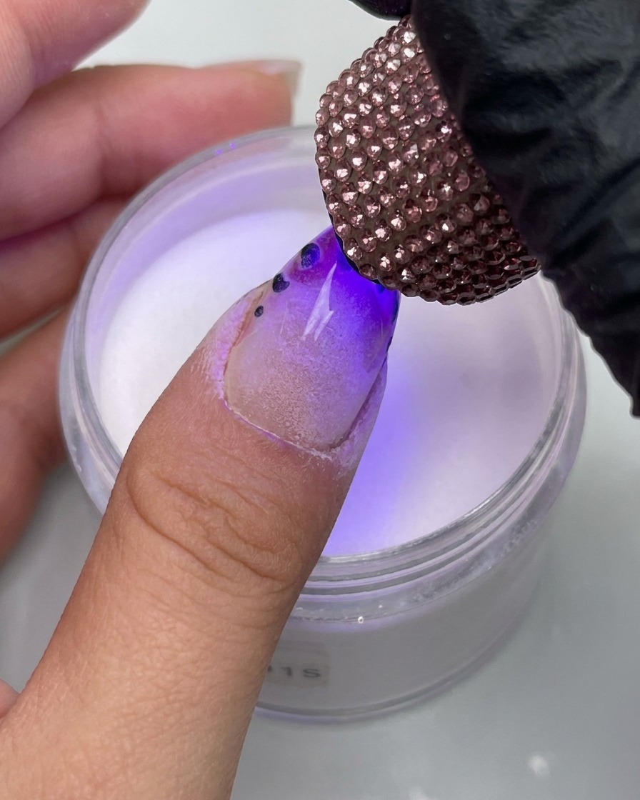 Nahaufnahme eines Fingers mit Leoparden-Design unter einer mit Strasssteinen verzierten UV-Lampe.