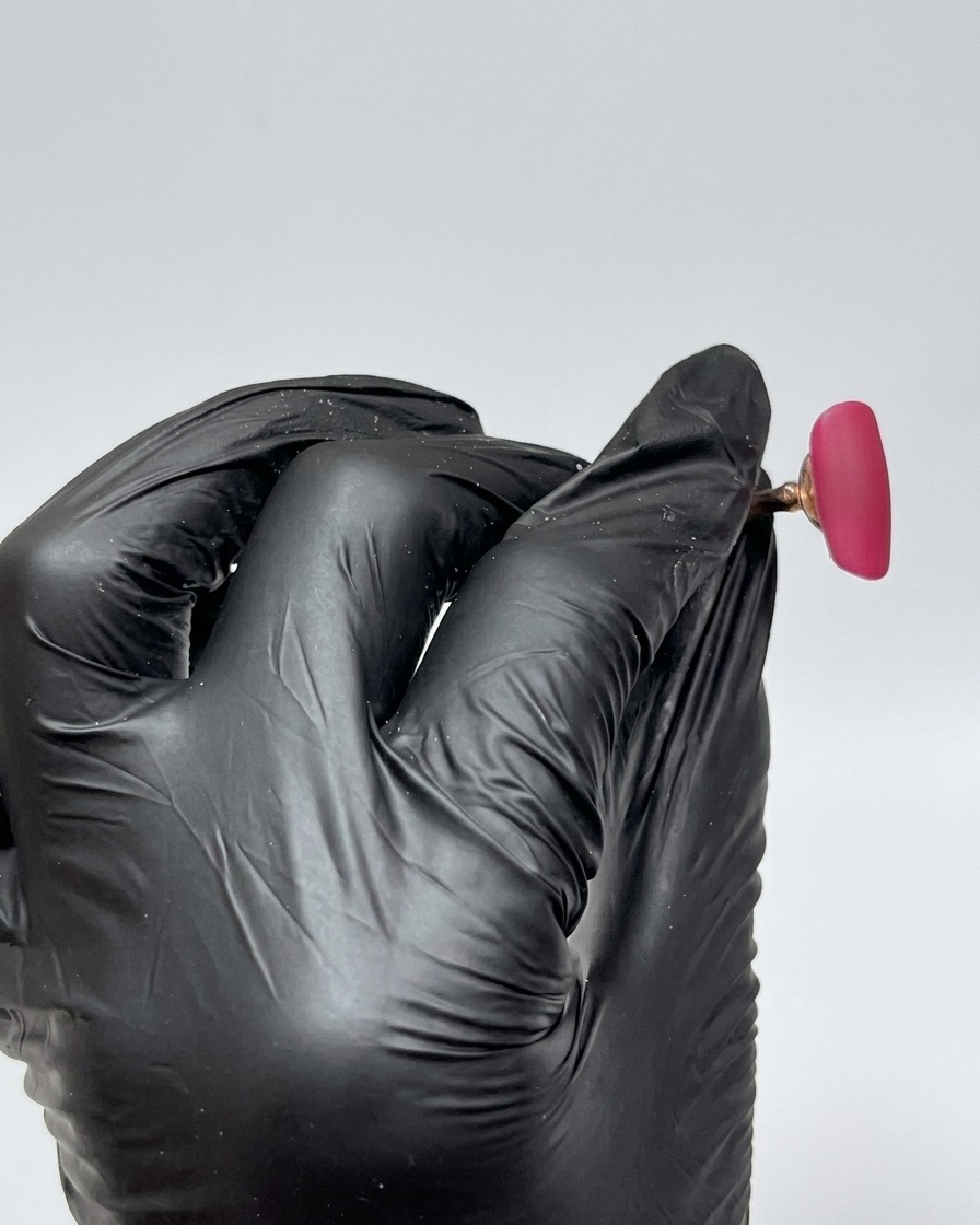 Nahaufnahme eines Nageltips, der vollständig mit einem leuchtend rosaroten Gel überzogen ist, mit einem glatten, glänzenden, noch nicht ausgehärteten Finish.