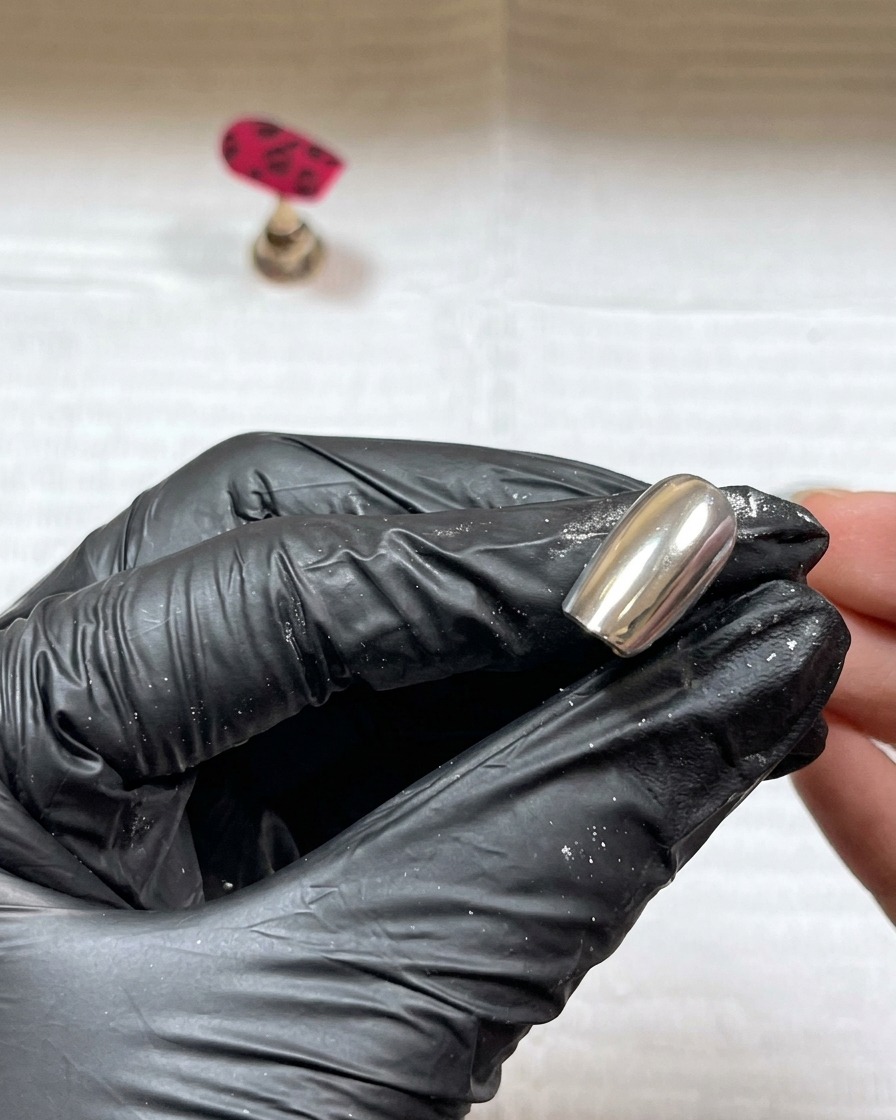 Klares Acrylpulver wird über die nassen schwarzen Gel-Details auf dem Nagel gestreut.