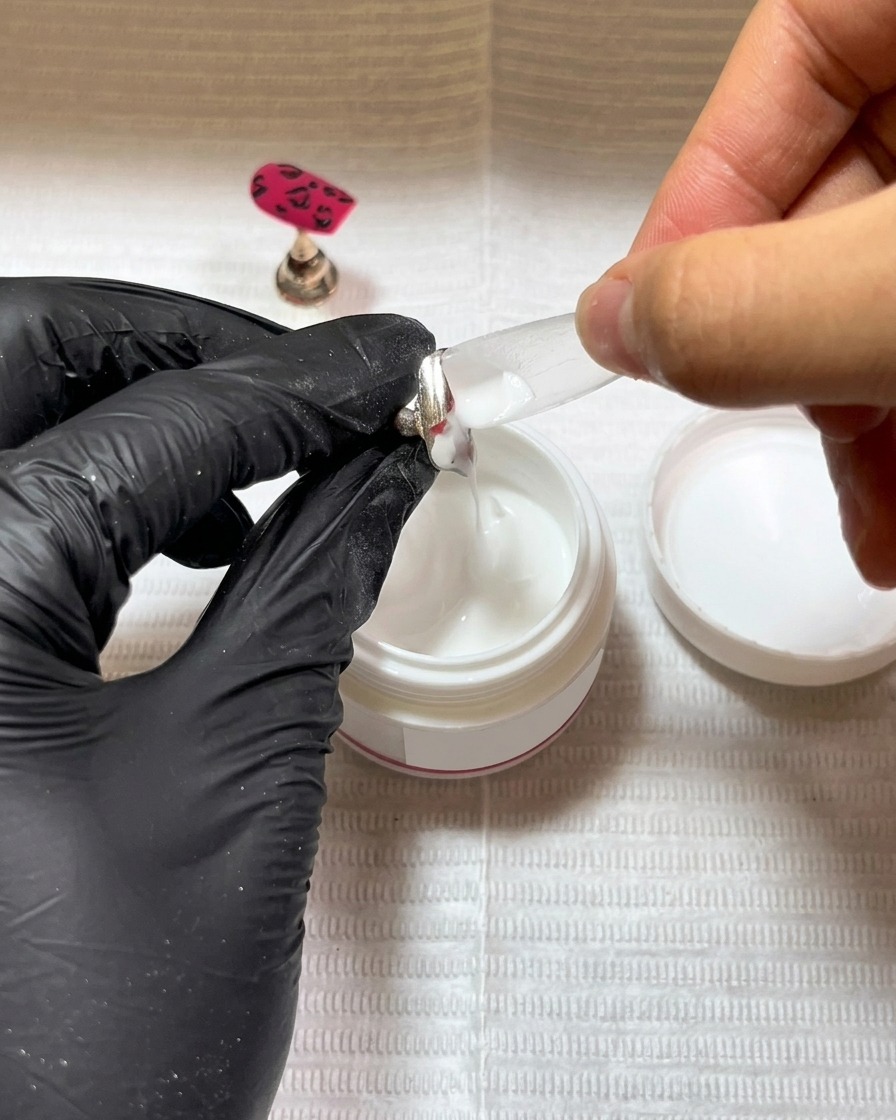 Ein Pinsel trägt eine dünne Schicht schwarzen Basisgels auf einen neuen Nageltip auf.