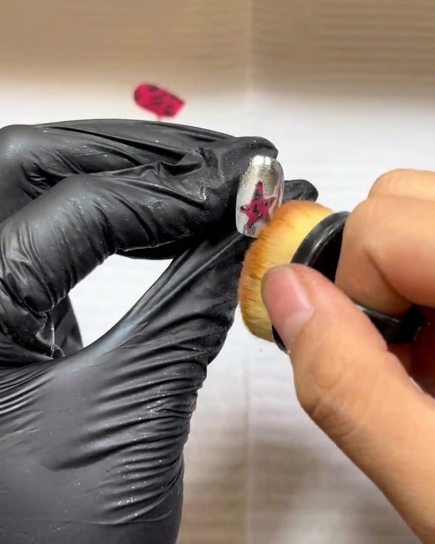 Ein kleiner Make-up-Pinsel wird verwendet, um überschüssiges Pulver sanft von einem strukturierten Sternen-Nageldesign zu fegen.