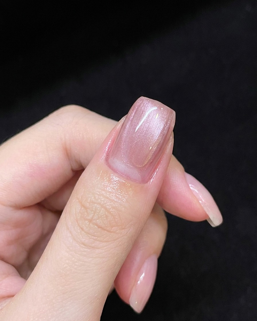 Eine Hand hält einen Magnetstab über den mit pinkem Gel beschichteten Nagel, um eine diagonale Schimmerlinie zu erzeugen.