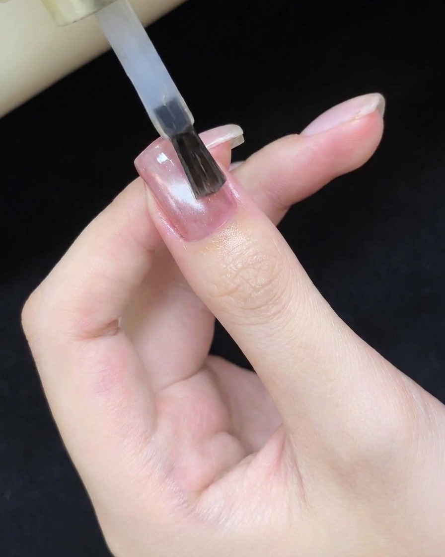Ein Pinsel trägt einen klaren, glänzenden Top-Coat auf das ausgehärtete Cat-Eye-Design auf.