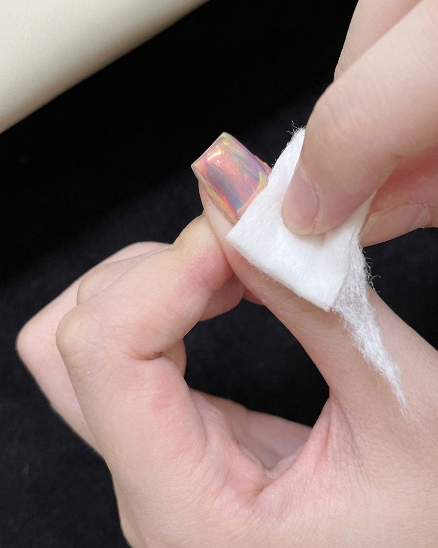 Ein Lidschatten-Applikator aus Schaumstoff reibt irisierendes Puder auf die glatte Nageloberfläche.