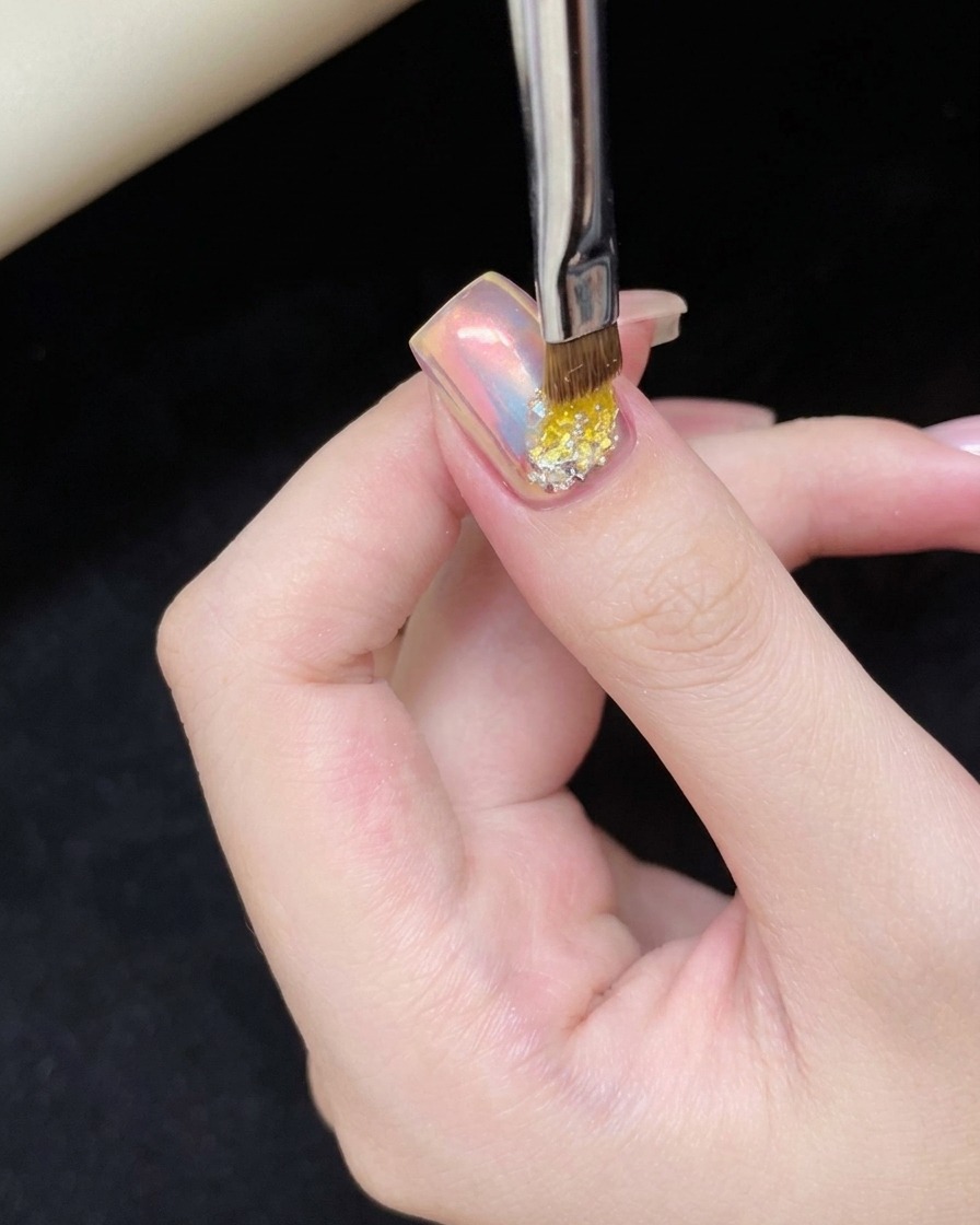 Ein kleiner Nagelpinsel trägt einen Tropfen Gel-Kleber auf den unteren Bereich des Cat-Eye-Nagels auf.