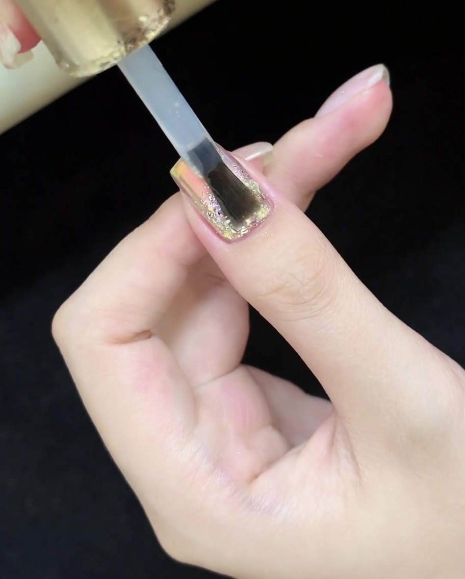 Ein Pinsel trägt einen klaren, glänzenden Top-Coat über das fertige Glitter- und Cat-Eye-Design auf.